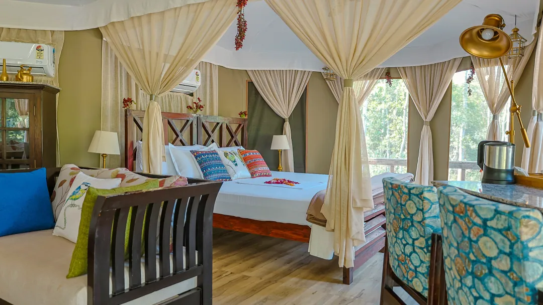 The bed in the Chief's Tent framed by draped curtains, with the forest beyond the windows